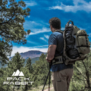 Hiker wearing green backpack looking out at mountains