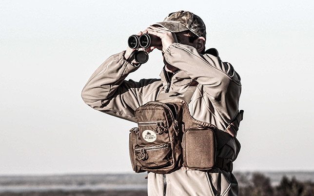 Man wearing tan chest pack looking through binoculars