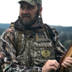 Turkey hunter wearing camouflaged chest pack using a turkey call