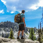 Hiker wearing green backpack looking at mountain