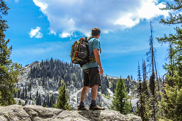 Hiker wearing green backpack looking at mountain