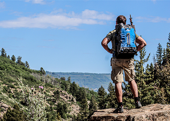 Hiker wearing blue backpack overlooking a valley