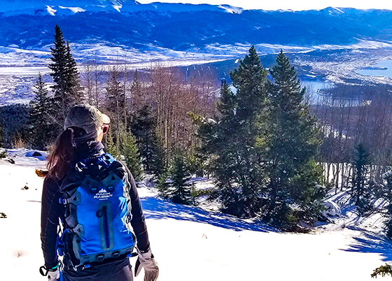 woman hiker wearing a blue backpack looking over a snow covered valley